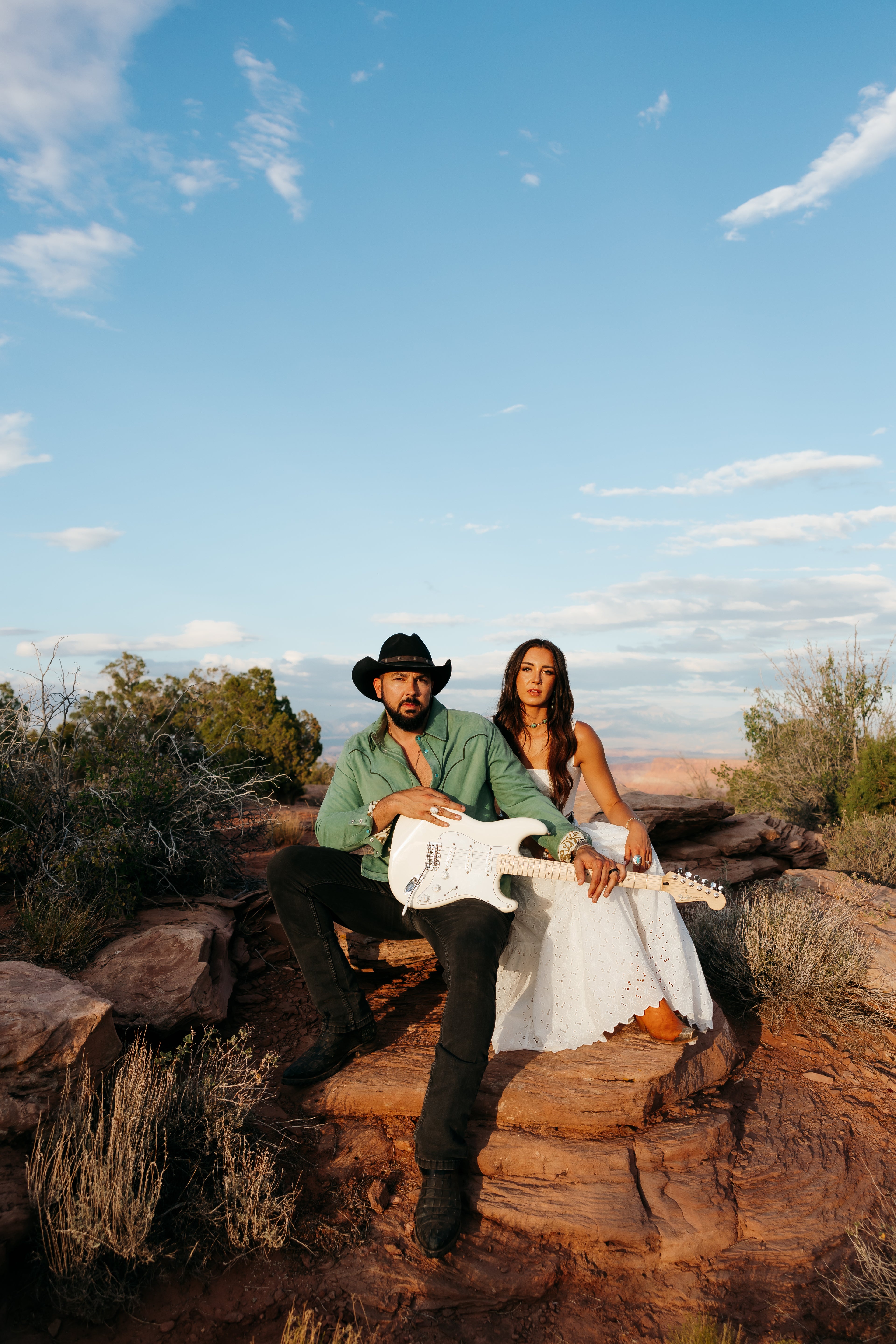 Country duo Tim & Taylor seated on red rock in the desert with an electric guitar