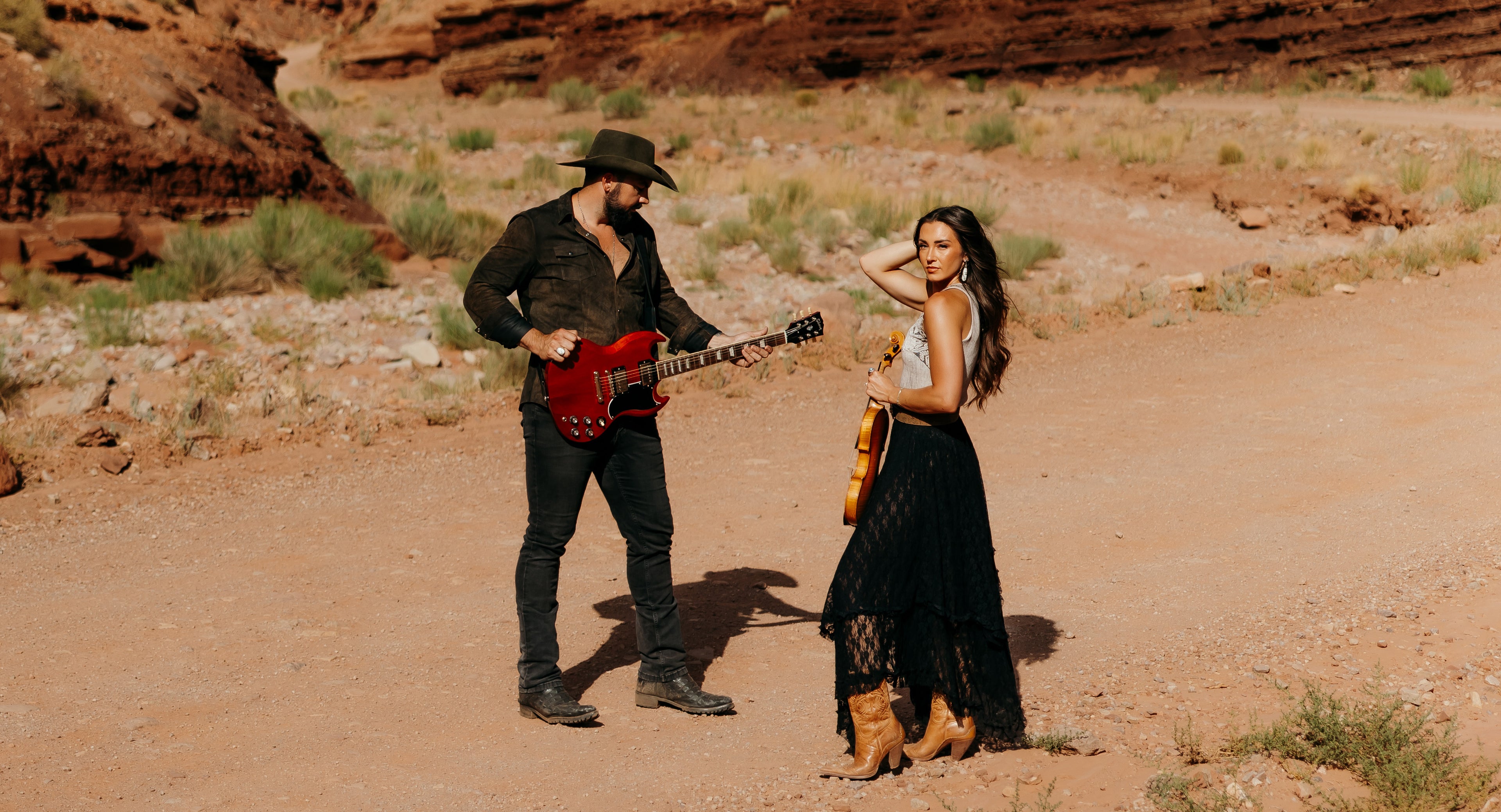 Country duo Tim & Taylor performing on a red rock desert road with electric guitar and fiddle