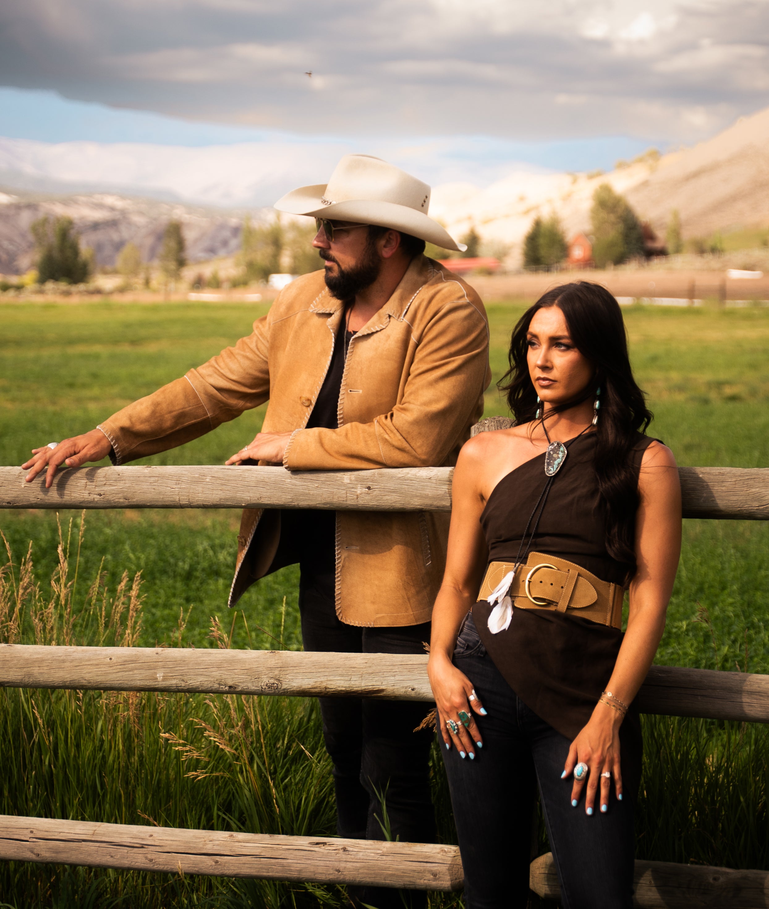 Country duo Tim & Taylor leaning on a wooden ranch fence with mountains behind them